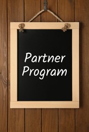 Image of Small black chalkboard with words Partner Program hanging on wooden wall