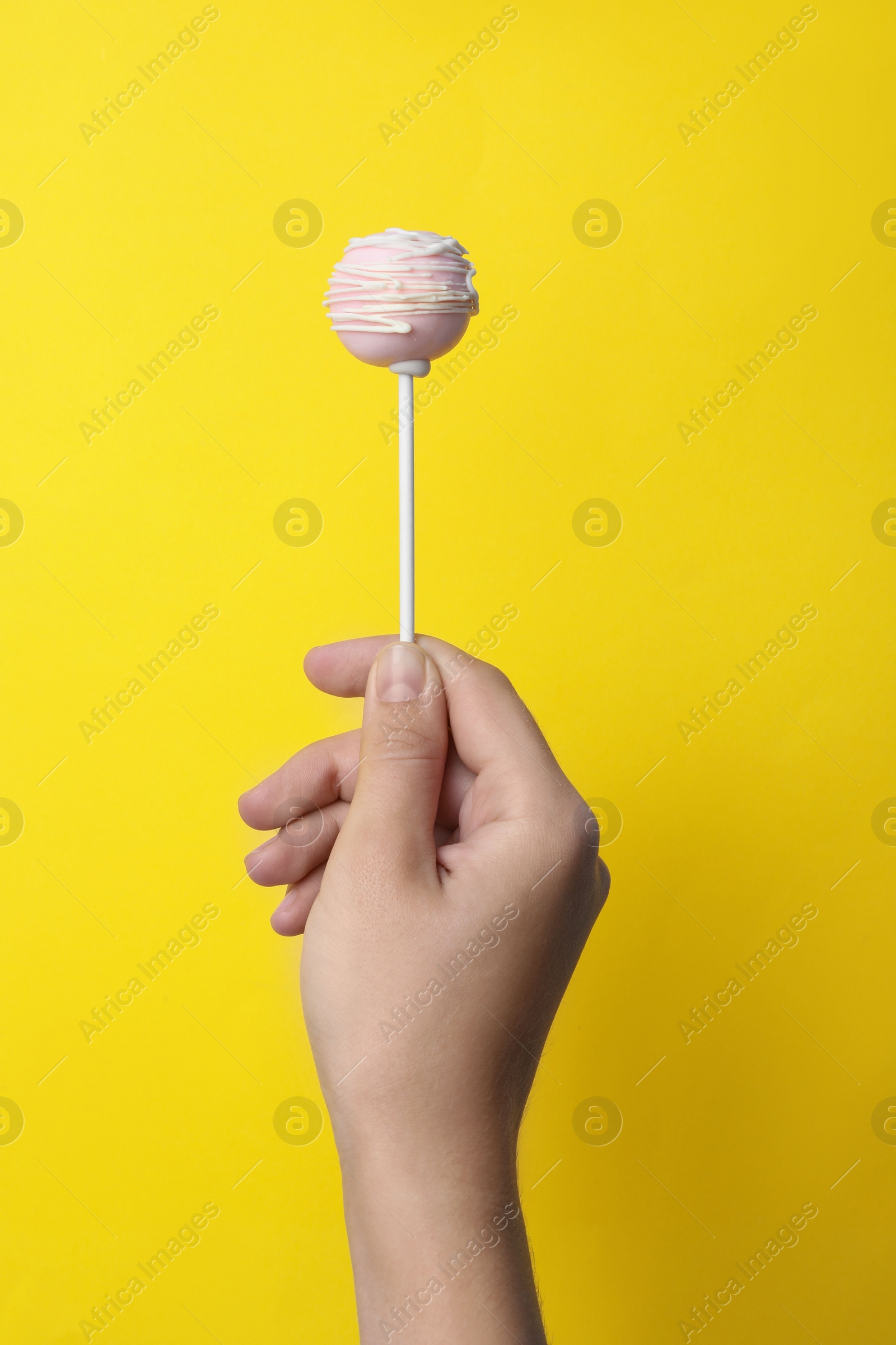 Photo of Woman holding sweet cake pop on yellow background, closeup