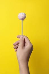 Woman holding sweet cake pop on yellow background, closeup