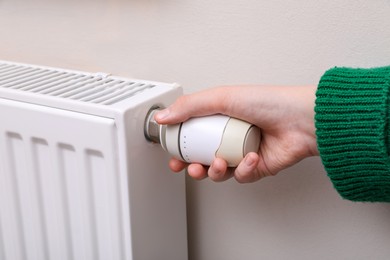 Photo of Girl adjusting heating radiator thermostat near white wall indoors, closeup