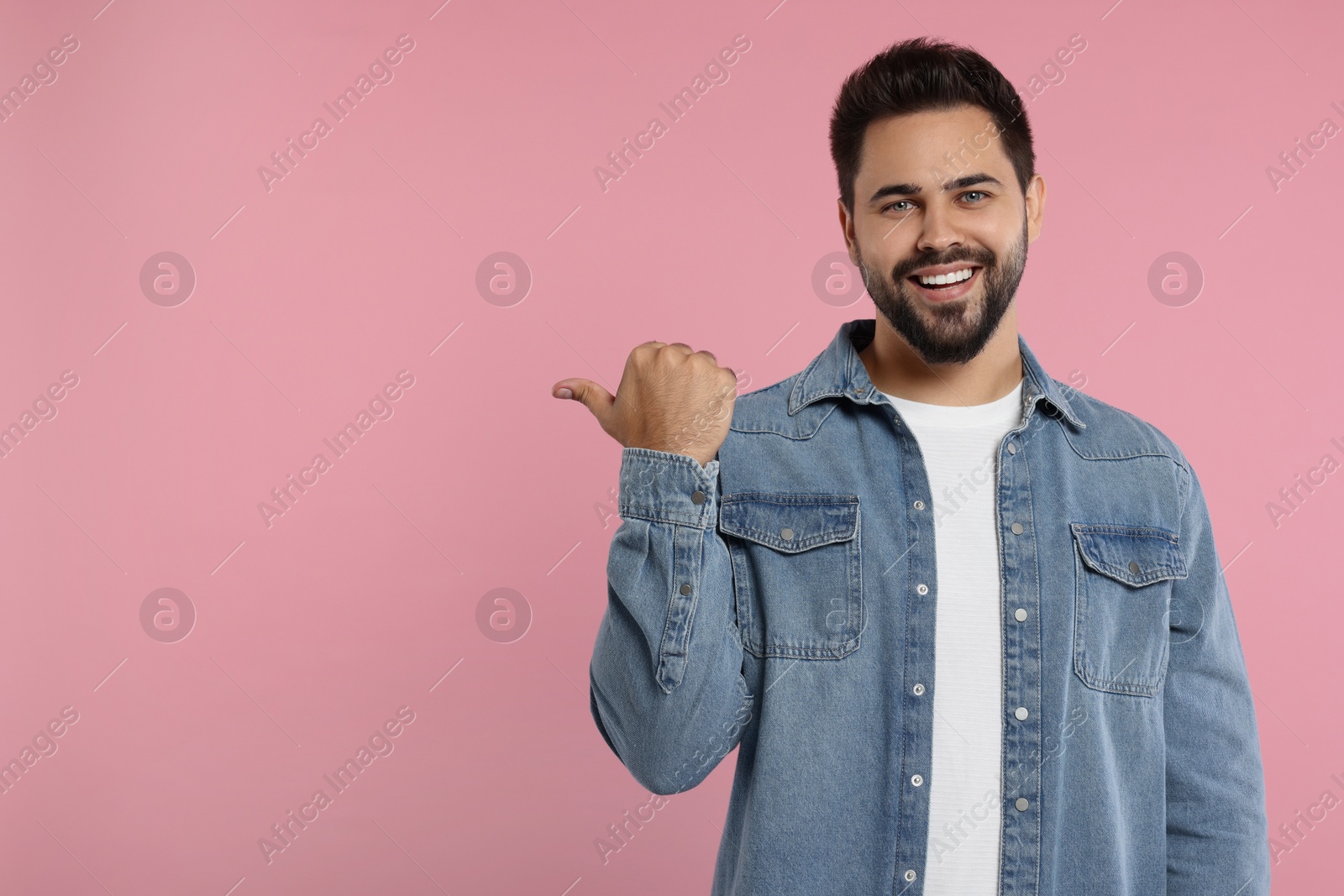 Photo of Special promotion. Smiling man pointing at something on pink background. Space for text