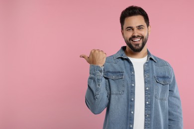 Photo of Special promotion. Smiling man pointing at something on pink background. Space for text