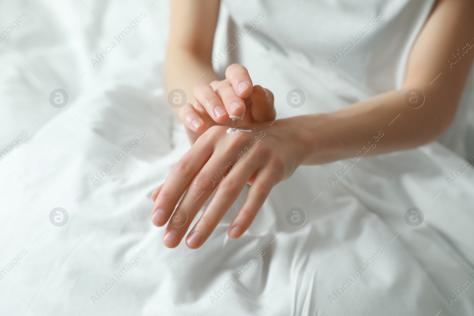 Photo of Woman applying hand cream in bed, closeup