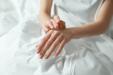 Photo of Woman applying hand cream in bed, closeup