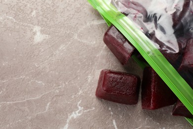 Frozen beet puree cubes in plastic bag on marble table, top view. Space for text