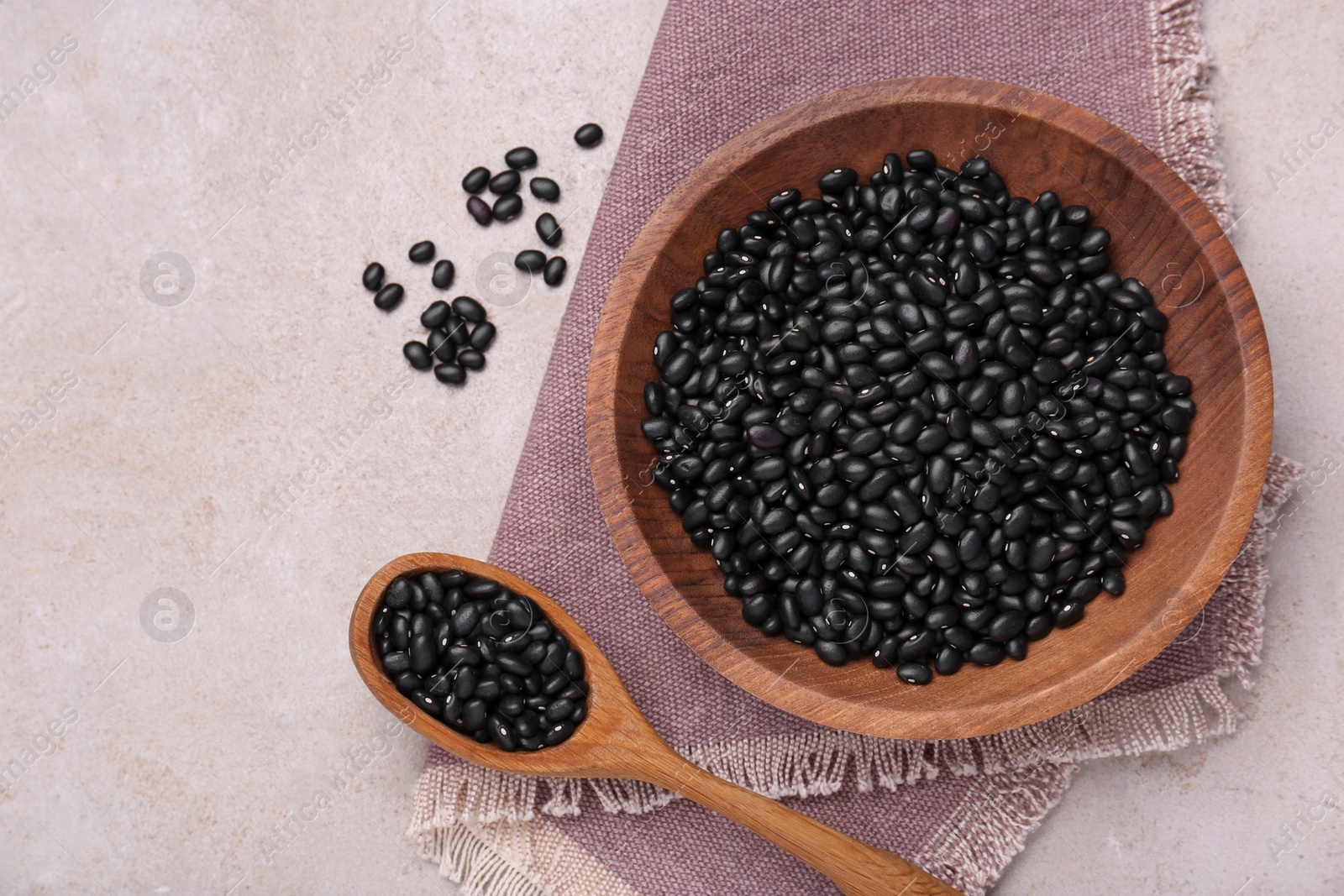 Photo of Bowl and spoon of raw black beans on light grey table, flat lay. Space for text