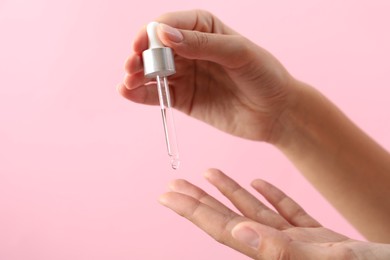 Photo of Woman applying cosmetic serum onto her finger on pink background, closeup