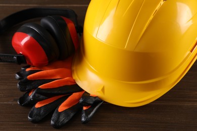 Hard hat, earmuffs and gloves on wooden table, closeup. Safety equipment