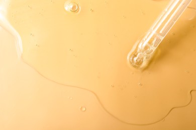 Photo of Dripping hydrophilic oil from pipette on beige background, top view