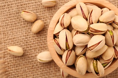Photo of Tasty pistachios in bowl on burlap fabric, top view. Space for text