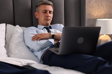 Photo of Businessman with laptop sleeping on bed indoors