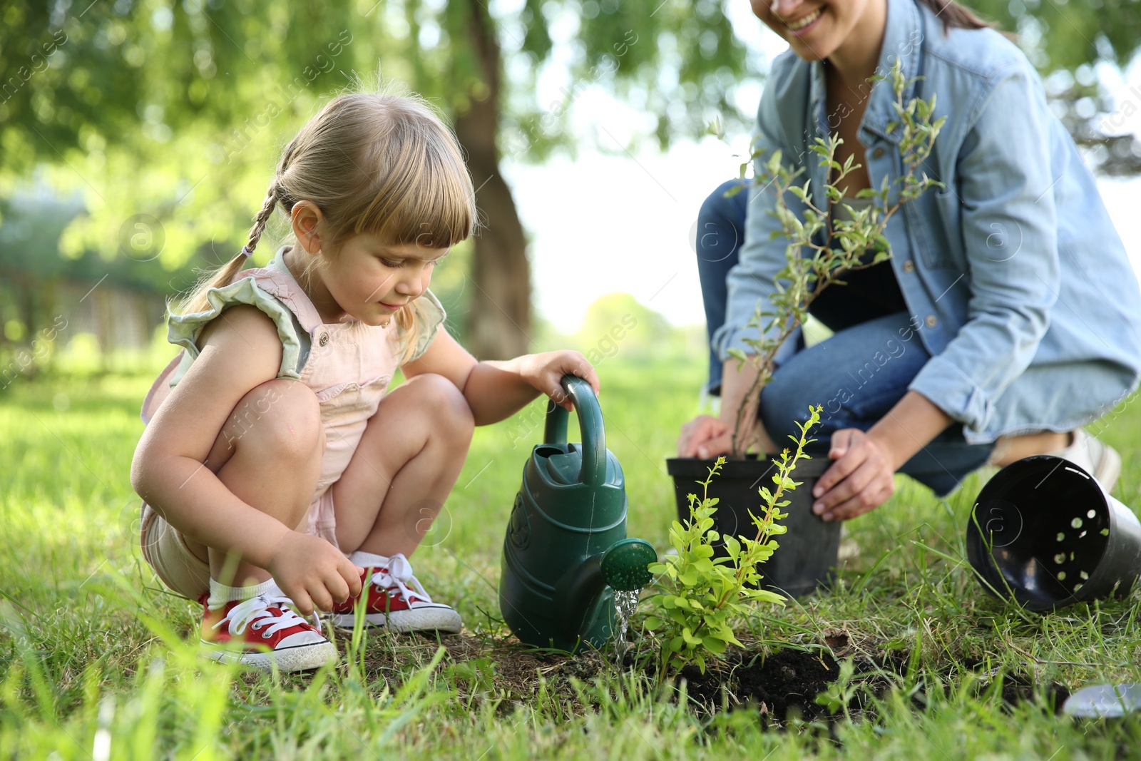 Photo of Mother and her daughter planting tree together in garden