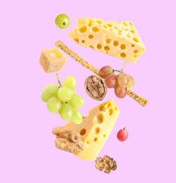 Cheese, breadstick, grapes and walnuts falling against violet background