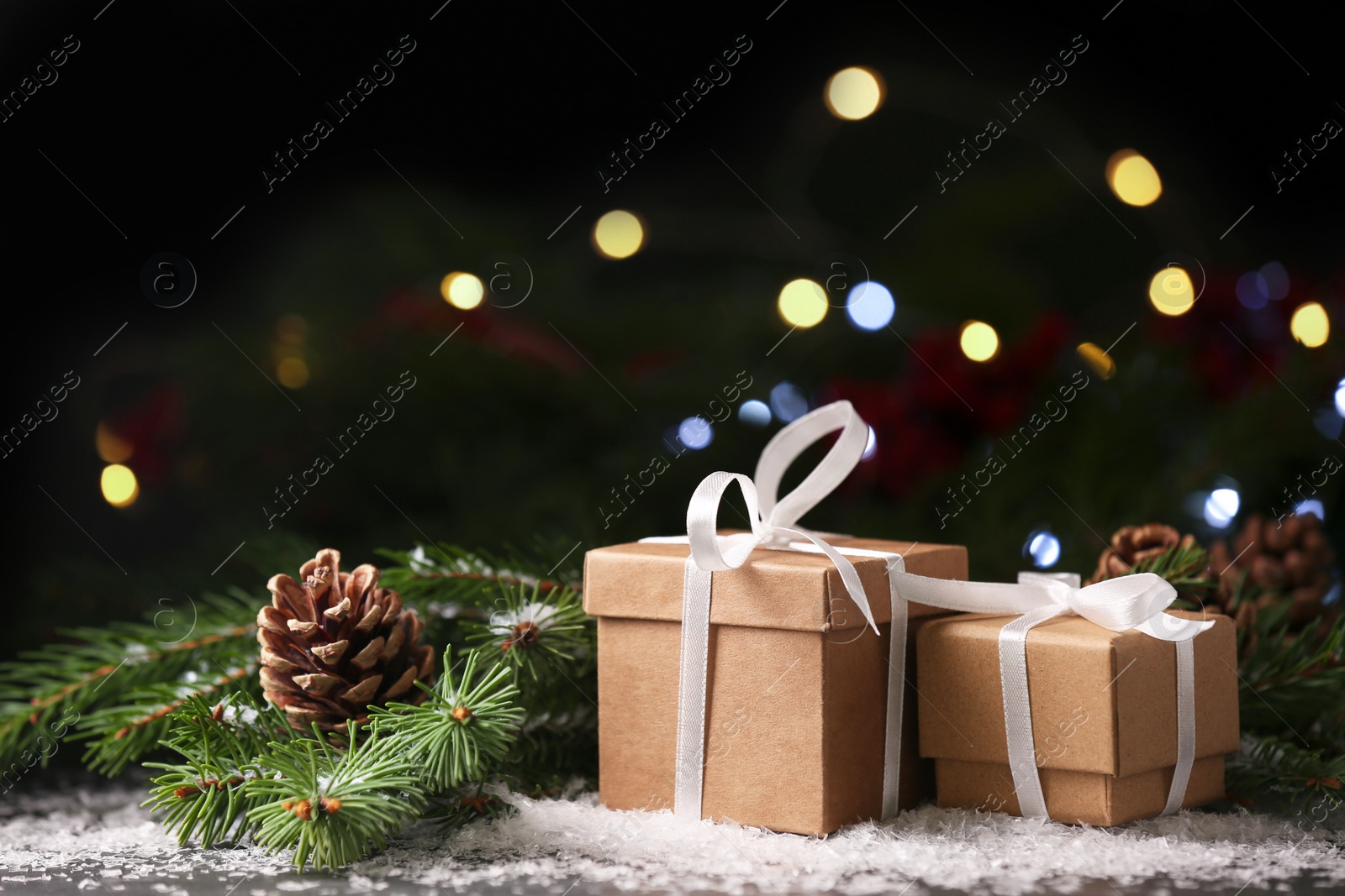 Photo of Christmas present. Beautiful gift boxes, artificial snow and fir tree branches on black table against blurred festive lights