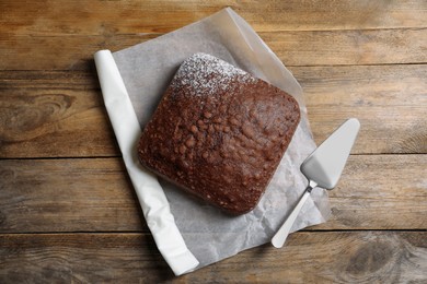 Photo of Homemade chocolate sponge cake and spatula on wooden table, flat lay