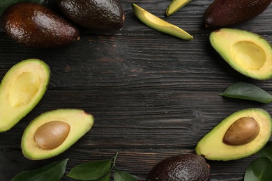 Photo of Frame of whole and cut avocados with green leaves on dark wooden table, flat lay. space for text