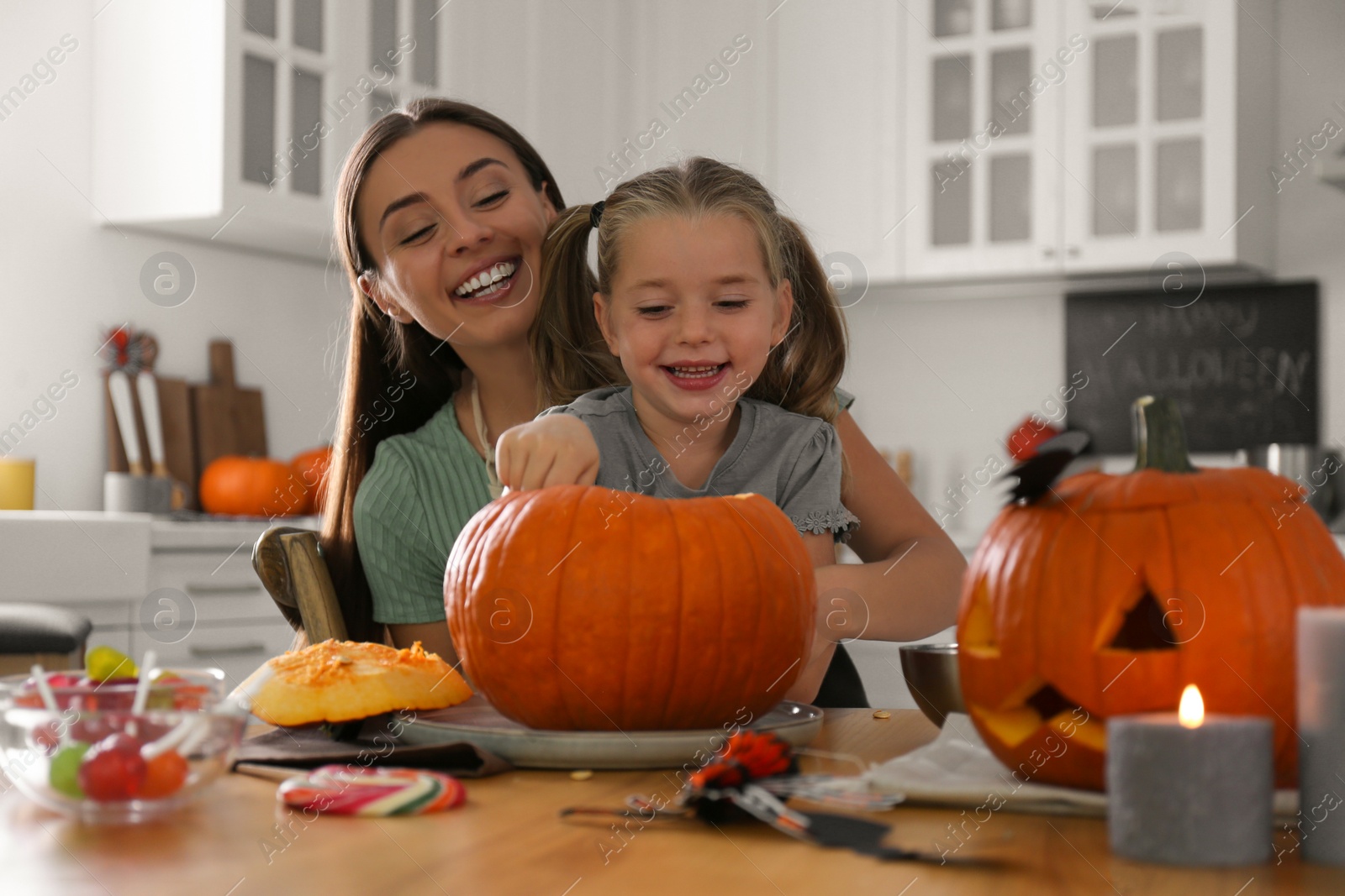 Photo of Mother and daughter making pumpkin jack o'lantern at table in kitchen. Halloween celebration