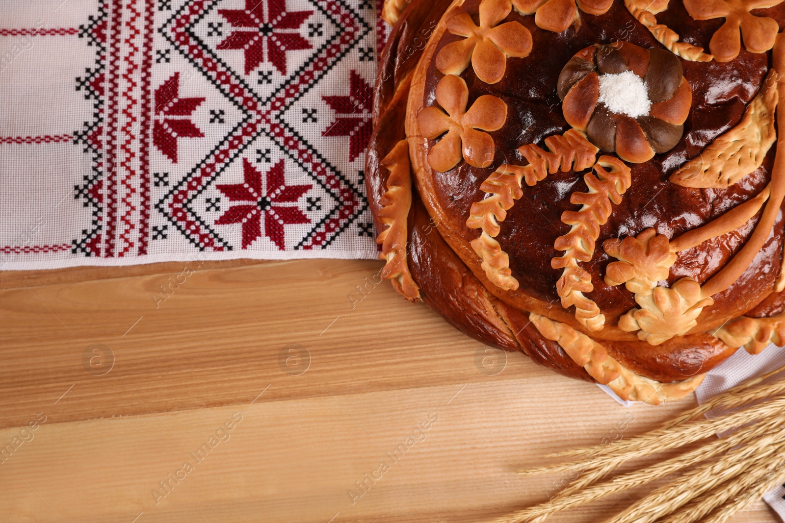 Photo of Rushnyk with korovai, wheat spikes on wooden table, flat lay. Ukrainian bread and salt welcoming tradition