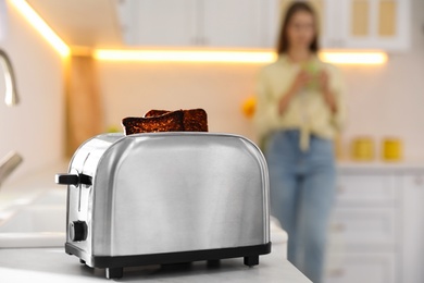 Modern toaster with slices of burnt bread and blurred woman on background