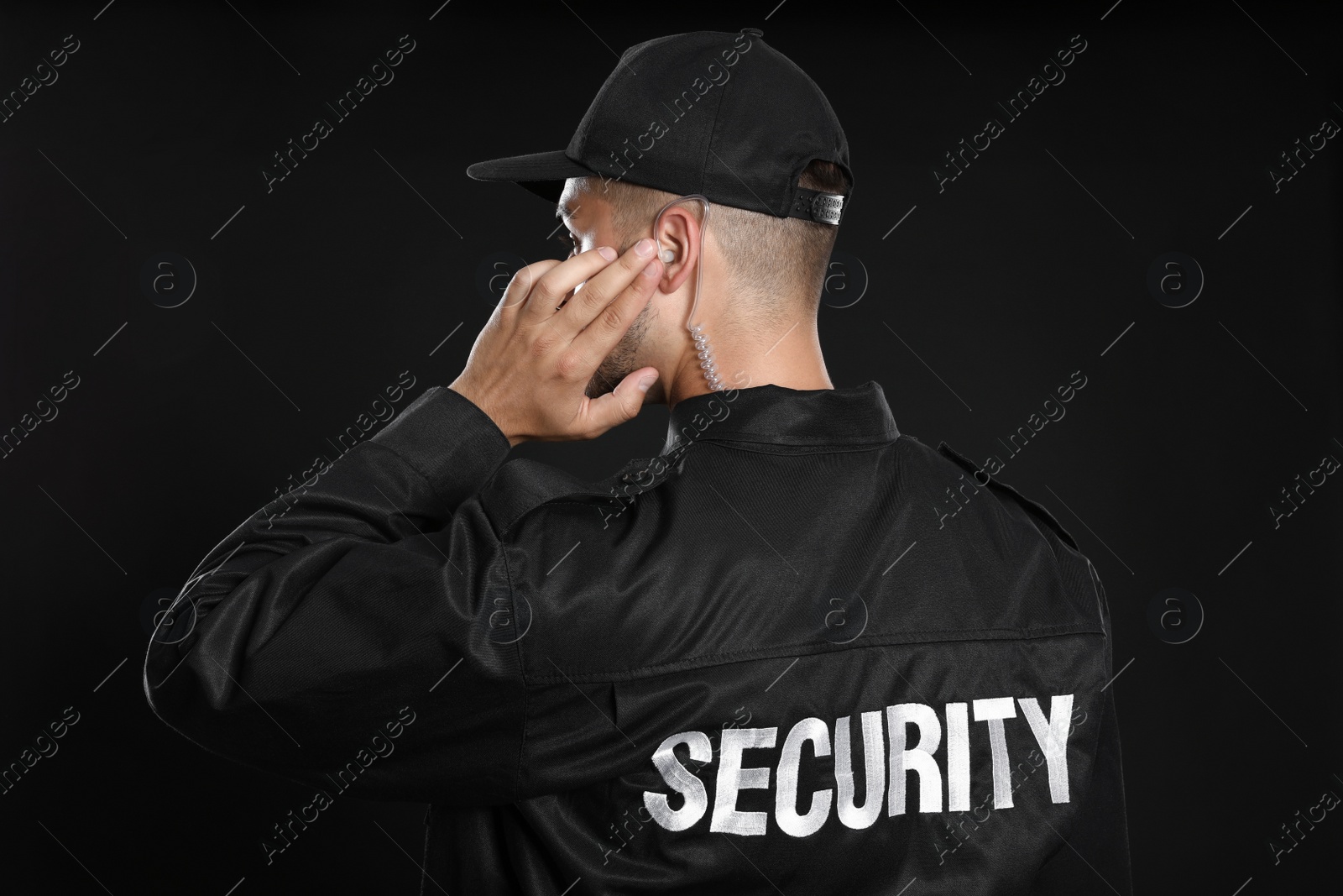 Photo of Male security guard in uniform using radio earpiece on dark background