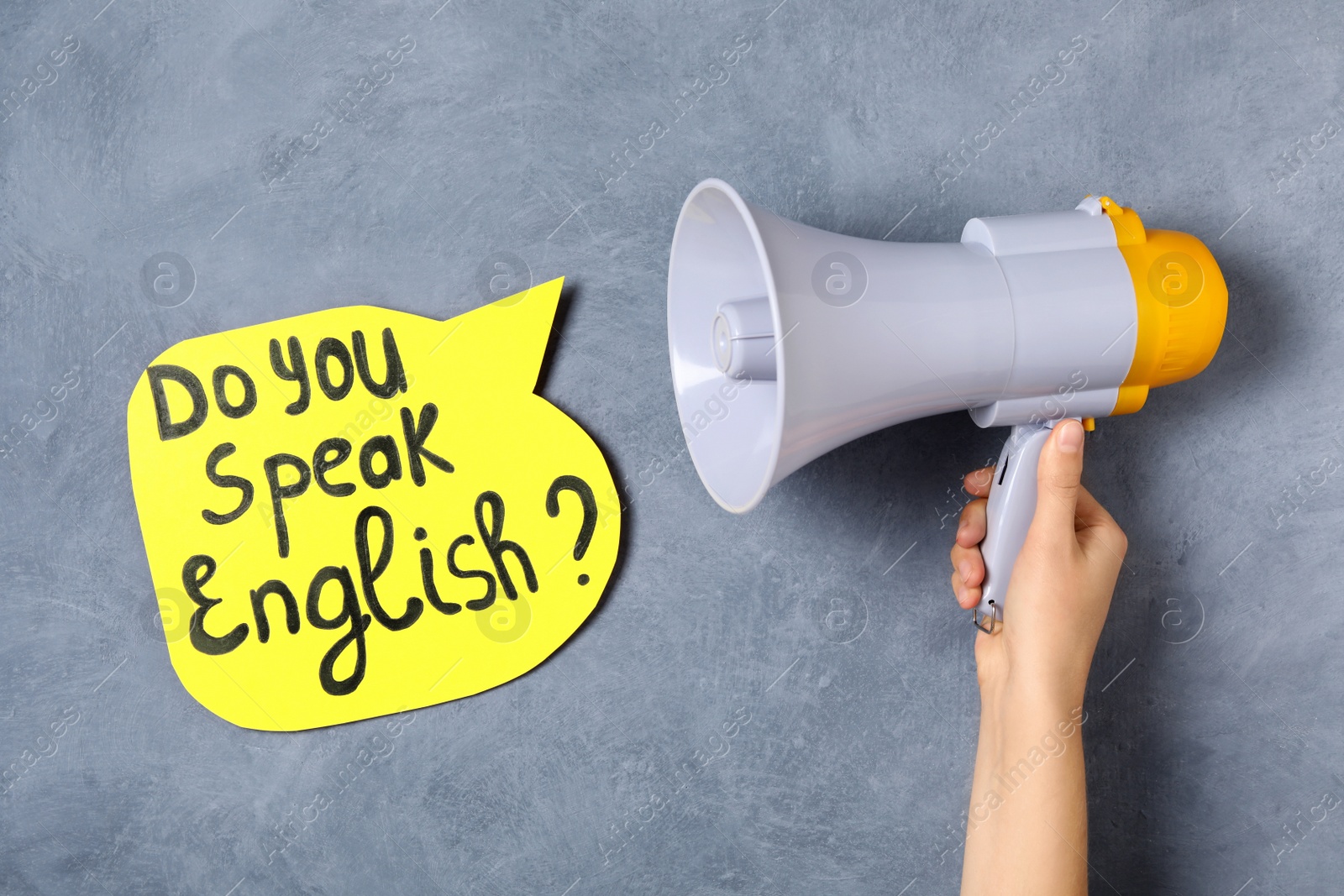 Photo of Woman holding horn and paper speech bubble with question Do You Speak English on grey background, closeup