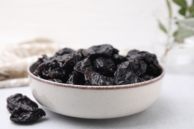 Photo of Bowl with sweet dried prunes on light table, closeup