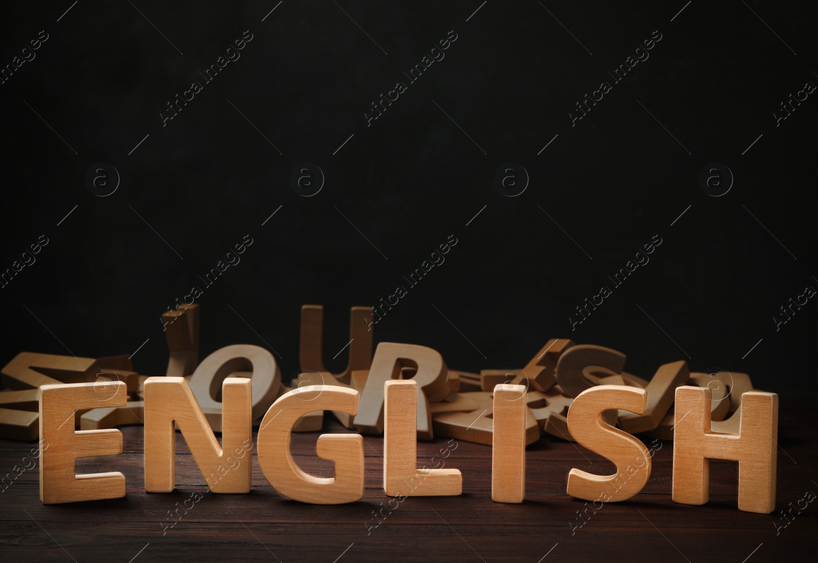 Photo of Word ENGLISH and pile of wooden letters on table against dark background. Space for text