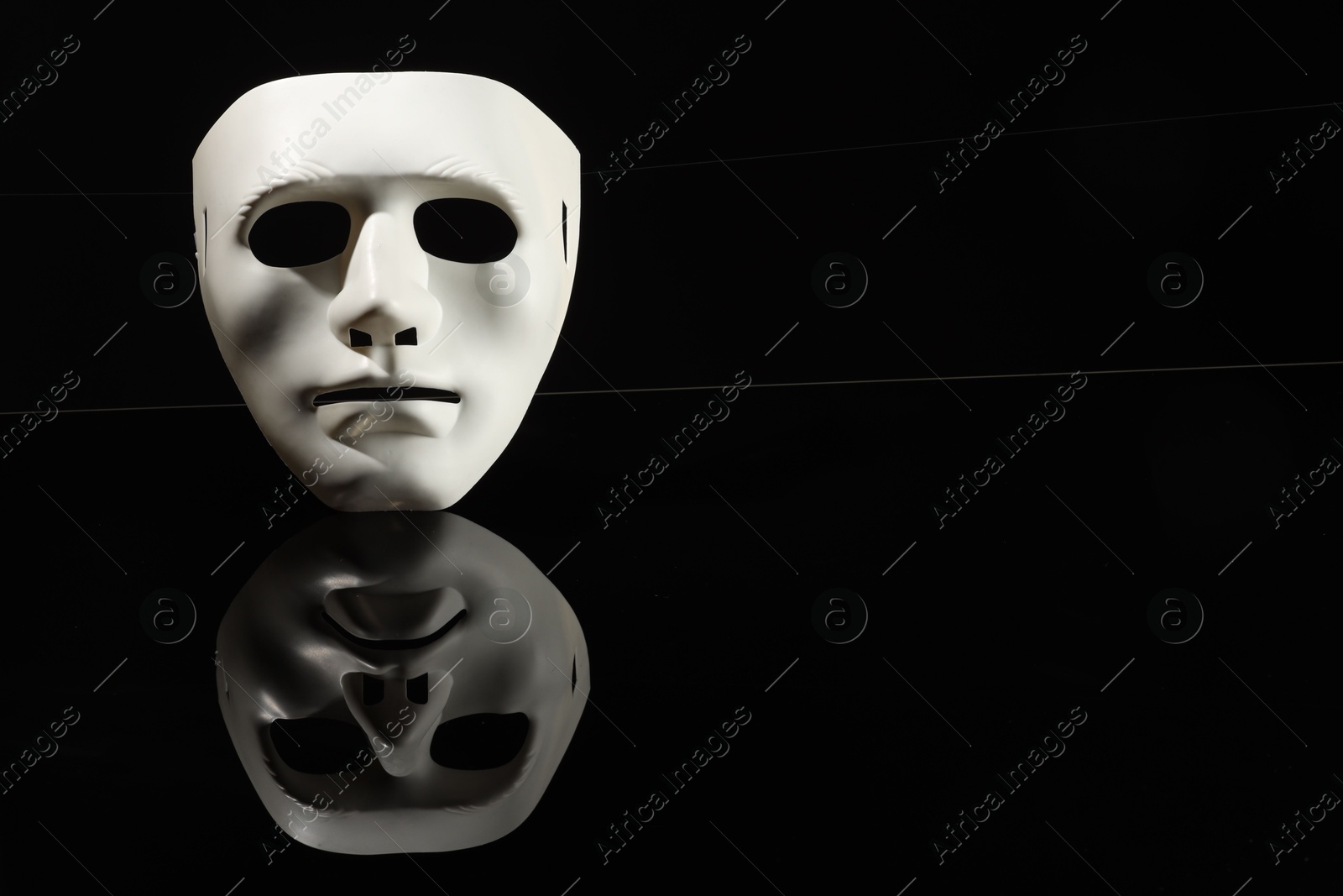 Photo of Plastic face mask on black mirror surface, space for text. Theatrical performance