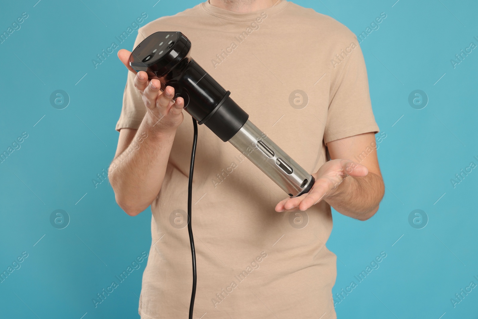 Photo of Man holding sous vide cooker on light blue background. closeup