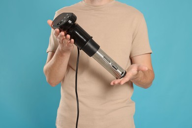 Man holding sous vide cooker on light blue background. closeup