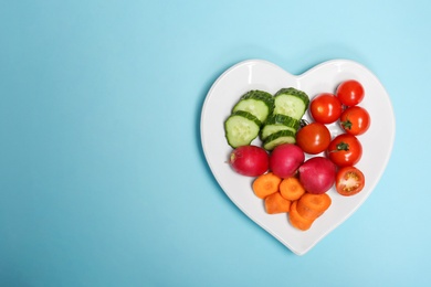 Photo of Heart shaped plate with fresh vegetables on color background, top view. Cardiac diet