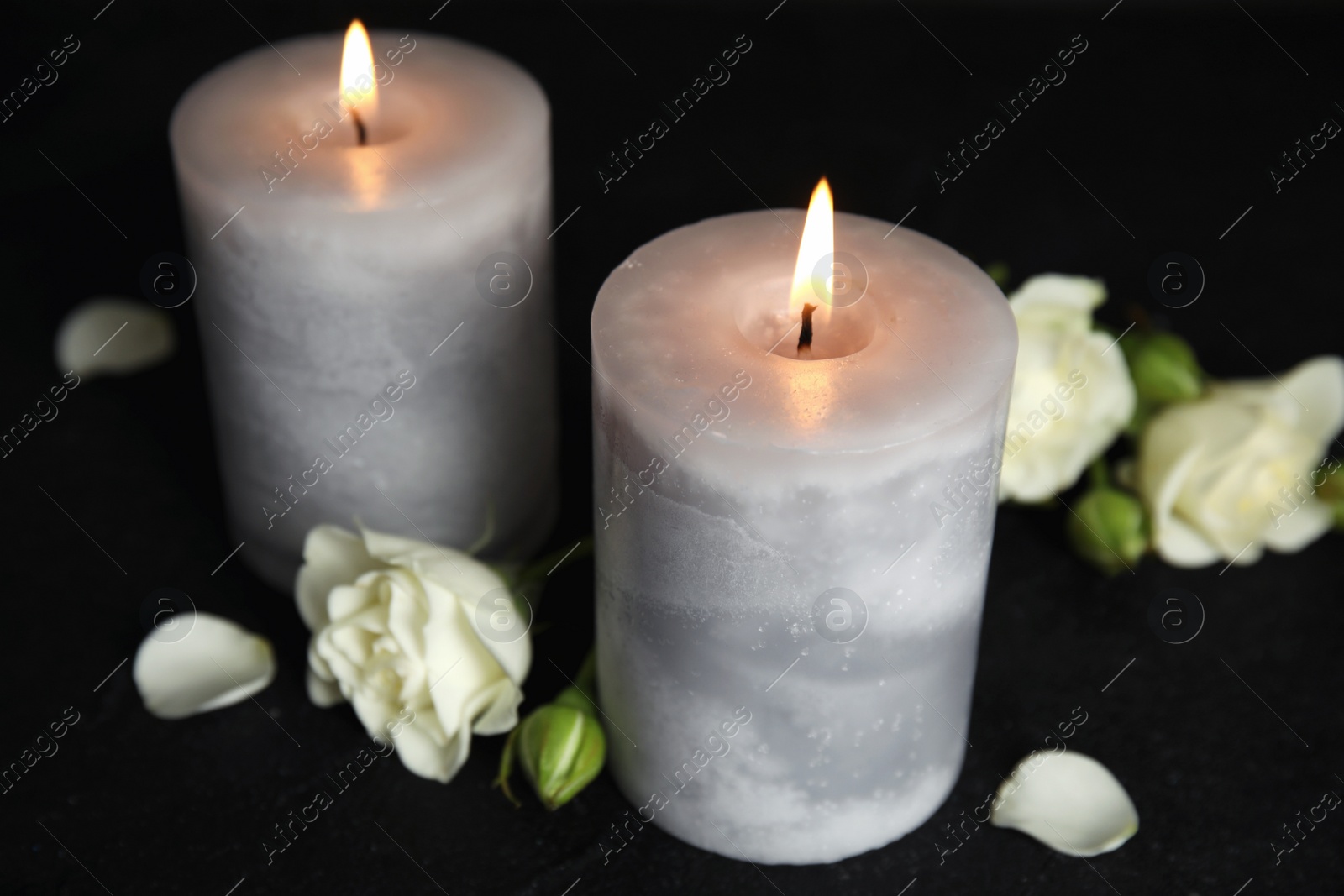 Photo of Burning candles and beautiful flowers on black table