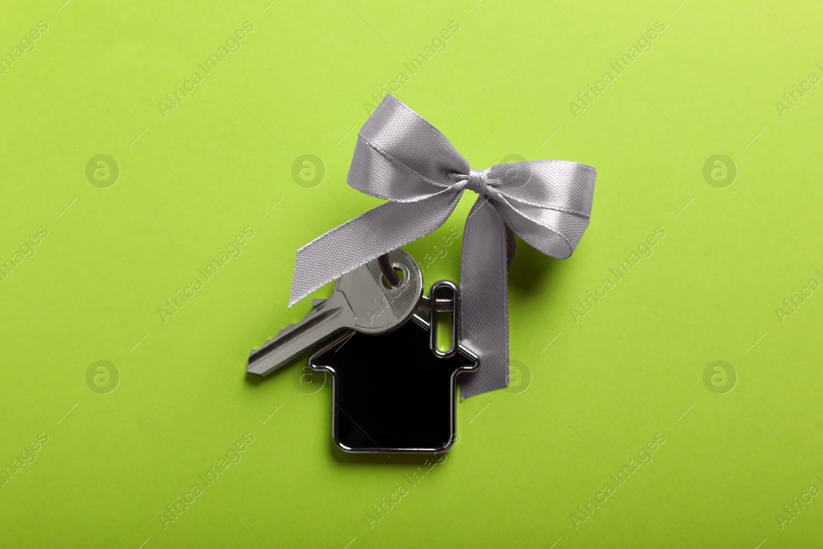 Photo of Key with trinket in shape of house and bow on light green background, top view. Housewarming party