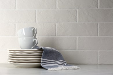 Soft kitchen towel and dishware on table near white brick wall, space for text