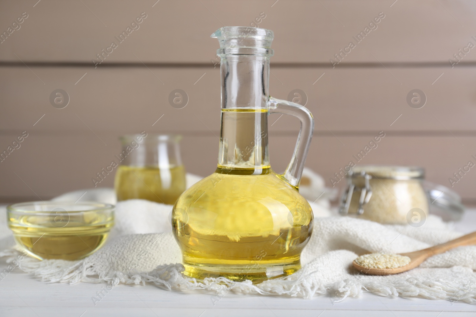 Photo of Jug of organic sesame oil and seeds on white wooden table