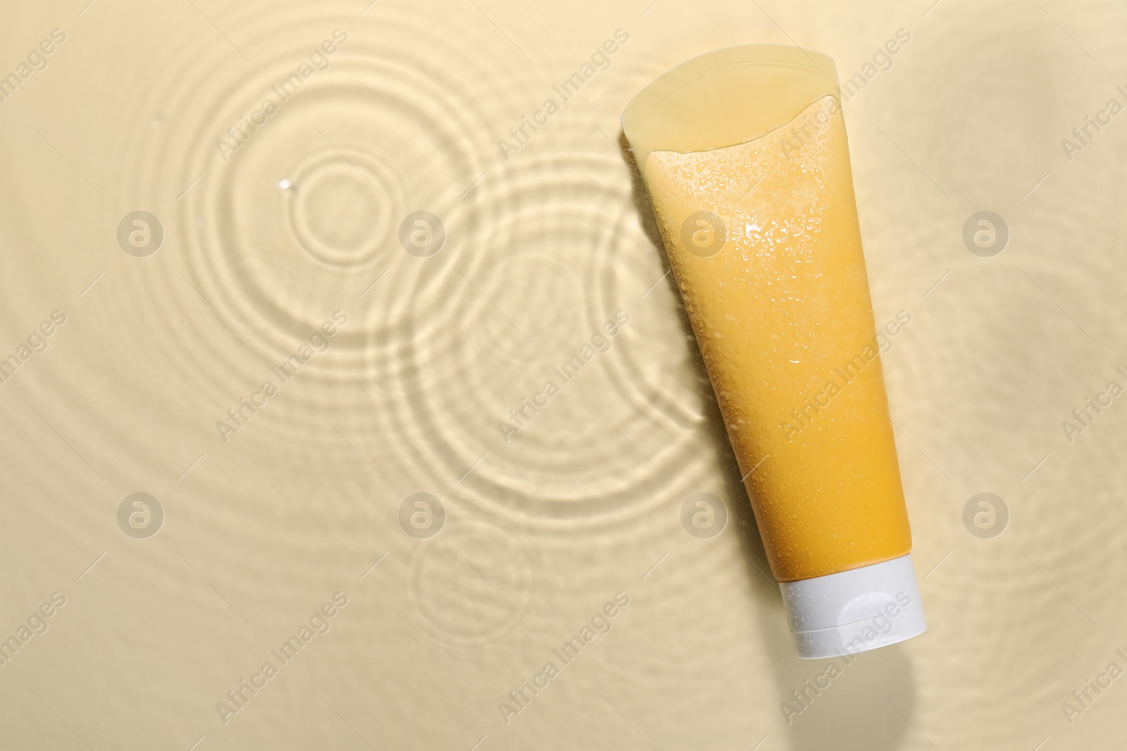 Photo of Tube of face cleansing product in water against beige background, top view. Space for text