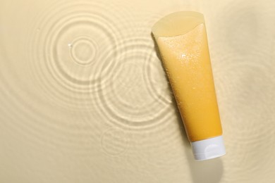 Photo of Tube of face cleansing product in water against beige background, top view. Space for text