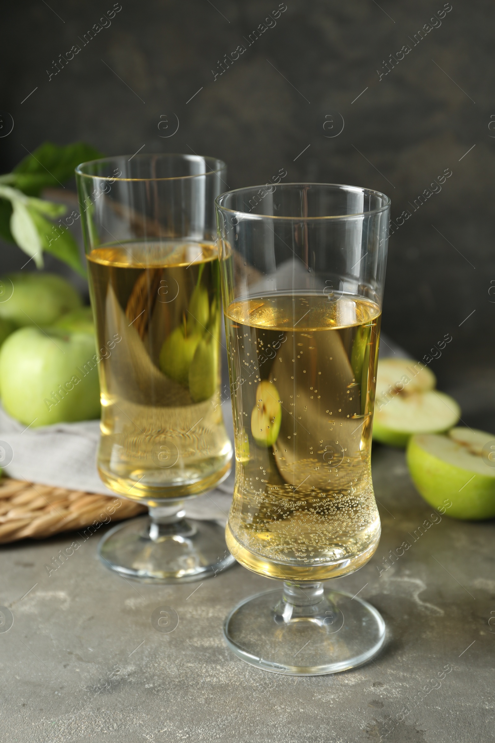 Photo of Glasses of delicious cider and green apples on gray table, closeup