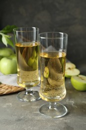 Photo of Glasses of delicious cider and green apples on gray table, closeup