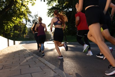 Photo of Group of people running outdoors on sunny day, back view