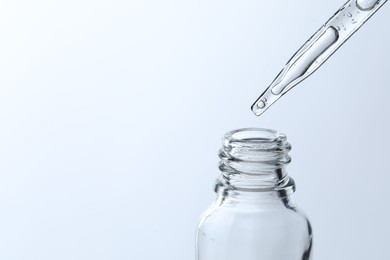 Dripping liquid from pipette into glass bottle on light blue background, closeup. Space for text