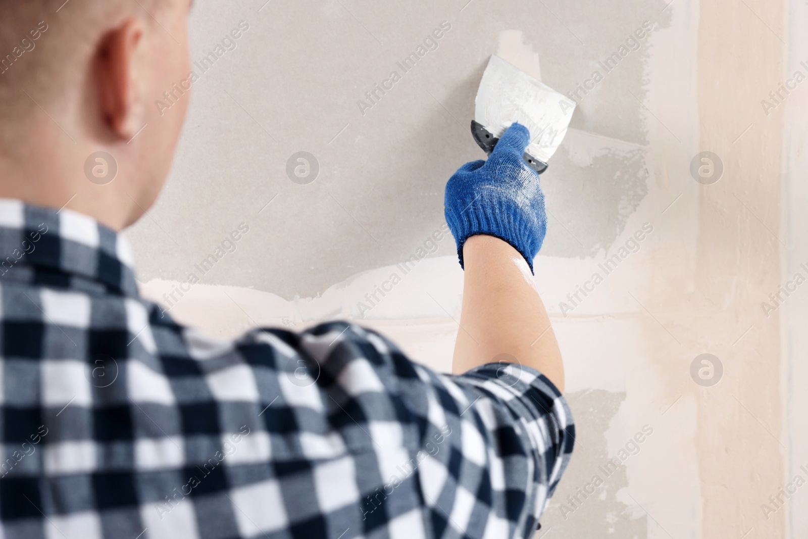 Photo of Man plastering wall with putty knife indoors, closeup. Home renovation