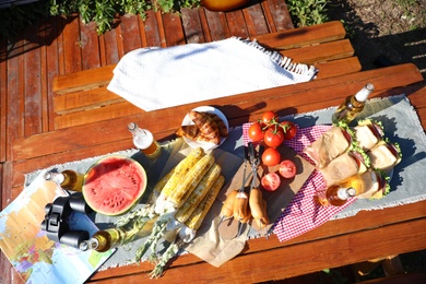 Photo of Bottles of beer, sandwiches and vegetables on wooden table, above view. Camping season