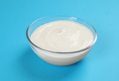 Photo of Bowl of tasty organic yogurt on light blue background