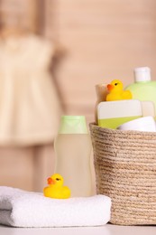 Wicker basket with baby cosmetic products, bath accessories and rubber ducks on table indoors