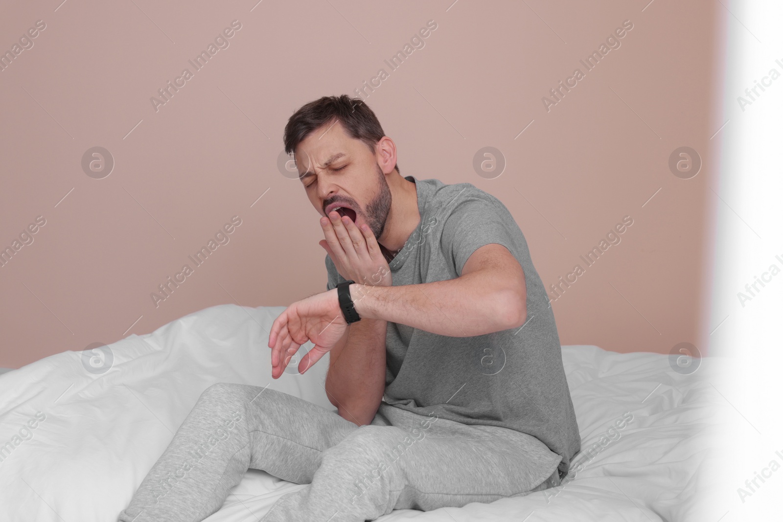 Photo of Sleepy man checking time on watch in bed at home