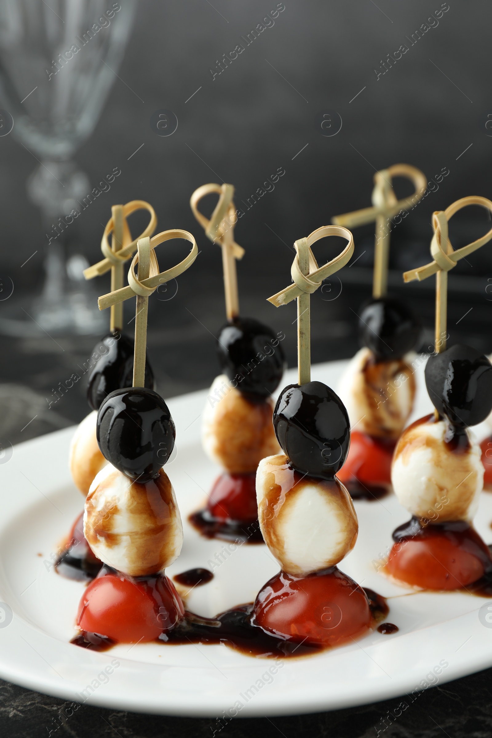 Photo of Tasty canapes with black olives, mozzarella and cherry tomatoes on dark textured table, closeup