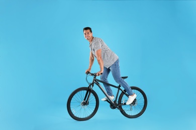 Handsome young man with modern bicycle on light blue background