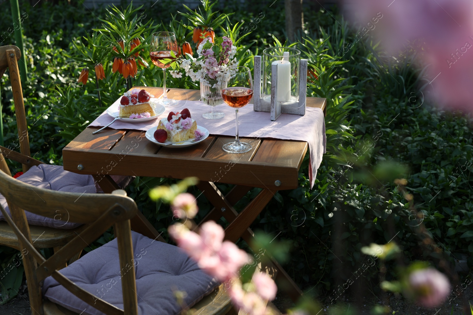 Photo of Vase with spring flowers, wine and cake on table served for romantic date in garden