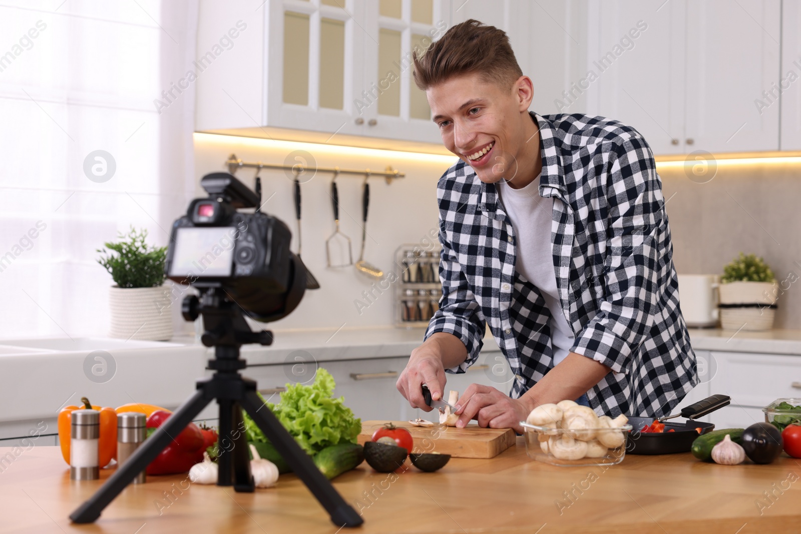 Photo of Smiling food blogger cooking while recording video in kitchen